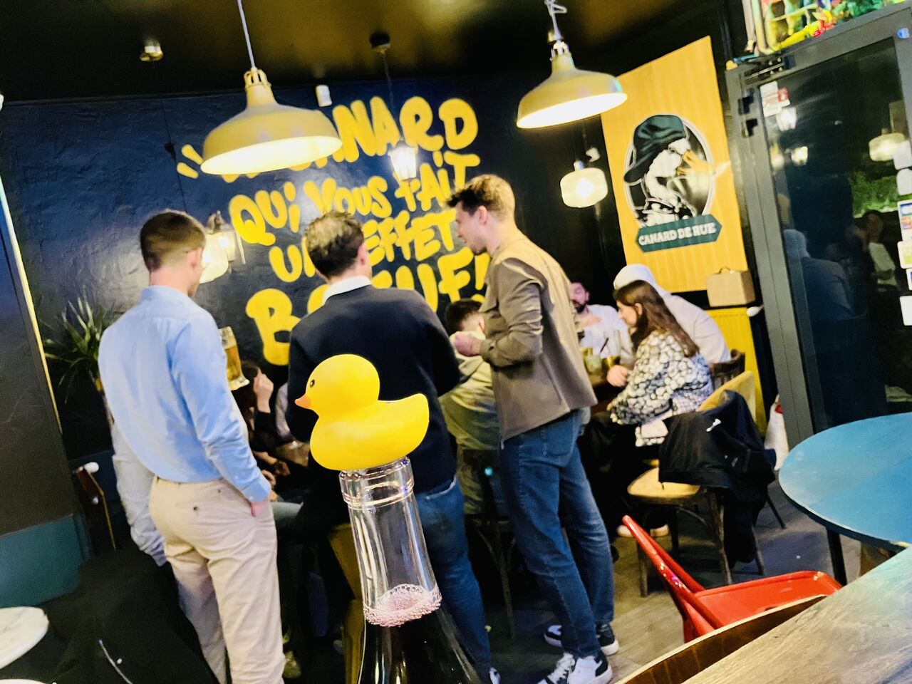 Le comptoir du Canard De Rue un soir de monde, verres à la main devant le mur peint